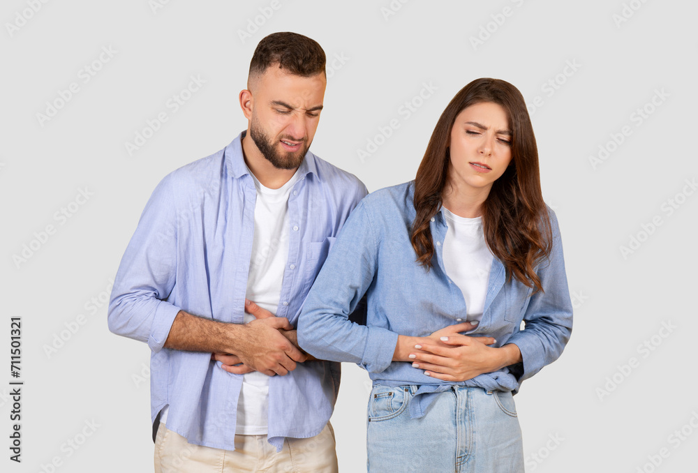 Couple with stomach ache, grimacing in discomfort on neutral background Couple with stomach ache, grimacing in discomfort on neutral background