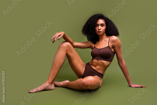 No filter photo of charming stunning girl with strong sportive body sitting on floor isolated over khaki color background
