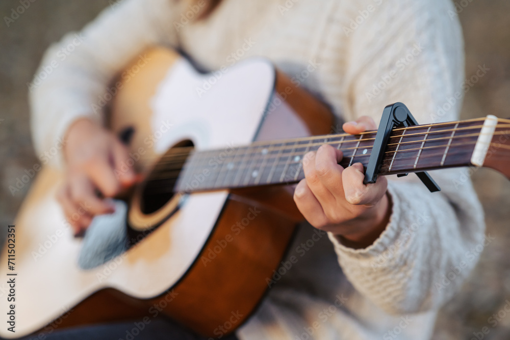 Guitar in hands of a young woman playing it. Playing music outdoors, using equipment capo - obrazy, fototapety, plakaty 