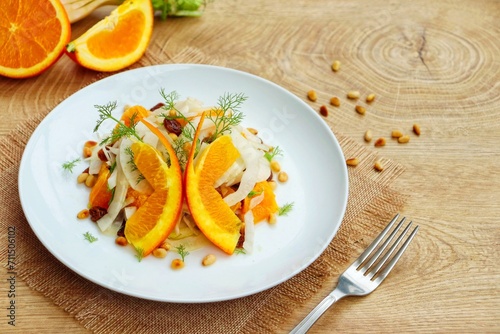 Italian Traditional Dish"Insalata di Finocchi e Arance" or "Fennel and Oranges Salad",fennel,oranges,raisins,pine nuts,olive oil,orange juice,salt and peppers on plate with wooden table.copy space