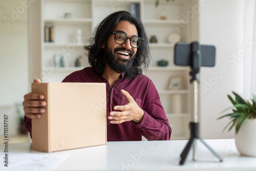 Indian influencer guy wearing glasses making video review of product at camera photo