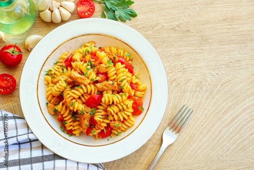 Italian Traditional Dish"Fusilli al tonno e pomodorini",fusilli pasta with canned tuna,cherry tomatoes,garlics,olive oil,parsley,salt and peppers on plate with wooden background.Top view.Copy space