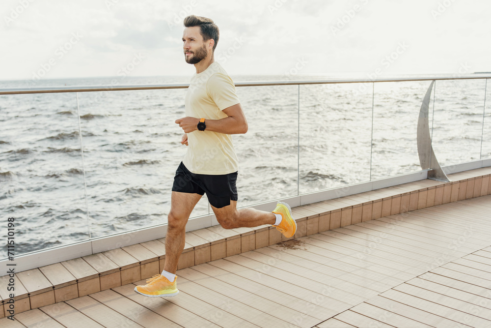 Man in sports gear running along the seashore on a wooden boardwalk, with waves in the background.