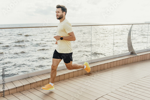 Man in sports gear running along the seashore on a wooden boardwalk, with waves in the background.