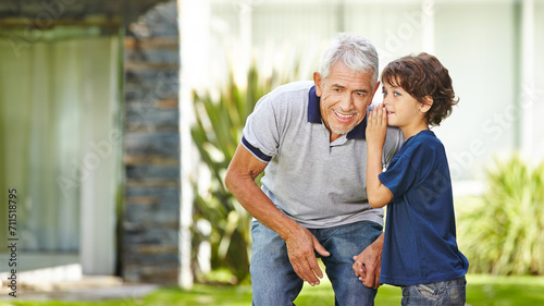Grandson whispering secret in ear of grandfather at home in garden