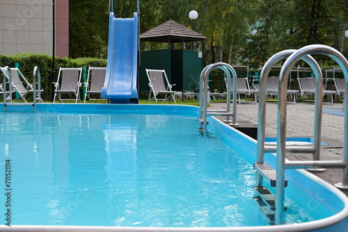 Shiny stainless steel swimming pool handrails next to the blue swimming pool The edge of the pool floor is covered with smart boards. There are many beds and pool chairs.