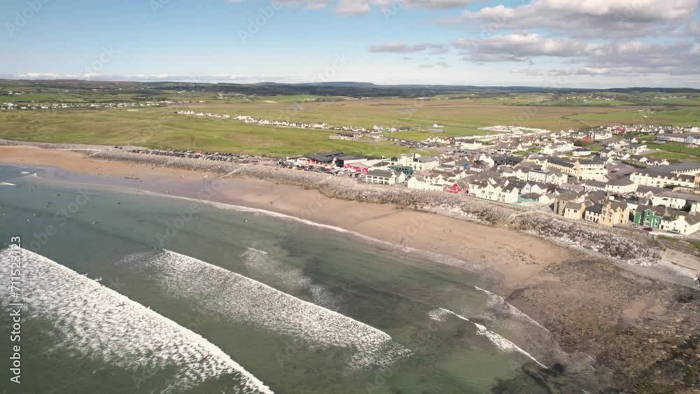 Aerial view on Lahinch beach and seafront buildings and busy car park. Warm sunny day with many surfers in the ocean on big waves. Popular tourist area. Cloudy sky. West of Ireland. Aerial view on Lahinch beach and seafront buildings and busy car park. Warm sunny day with many surfers in the ocean on big waves. Popular tourist area. Cloudy sky. West of Ireland.
