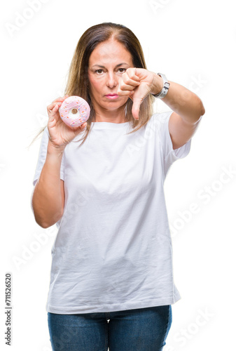 Middle age hispanic woman eating pink donut over isolated background with angry face, negative sign showing dislike with thumbs down, rejection concept