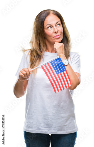 Middle age hispanic woman holding flag of United States of America over isolated background serious face thinking about question  very confused idea