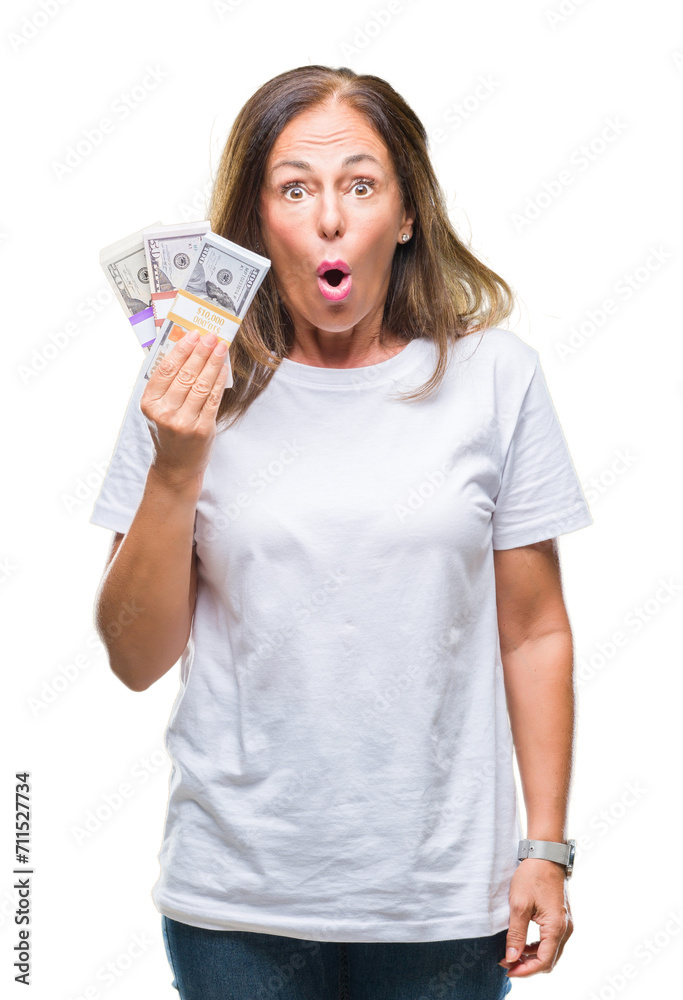 Middle age hispanic woman holding bunch of dollars over isolated background scared in shock with a surprise face, afraid and excited with fear expression Middle age hispanic woman holding bunch of dollars over isolated background scared in shock with a surprise face, afraid and excited with fear expression