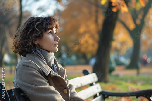 Woman on a park bench in autumn - holding a locket as a memento - deep in thought - reflecting on memories of a departed loved one. photo
