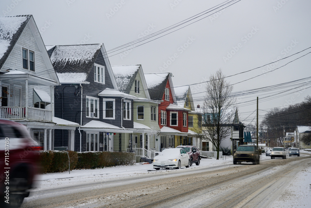 New England Winter Street with sand, slush, and snow on the road as cars crawl slowly pass mid-century style city houses in January