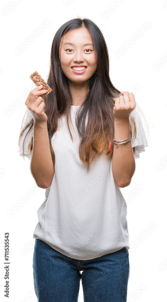 Young asian woman eating chocolate energetic bar over isolated background screaming proud and celebrating victory and success very excited, cheering emotion Young asian woman eating chocolate energetic bar over isolated background screaming proud and celebrating victory and success very excited, cheering emotion