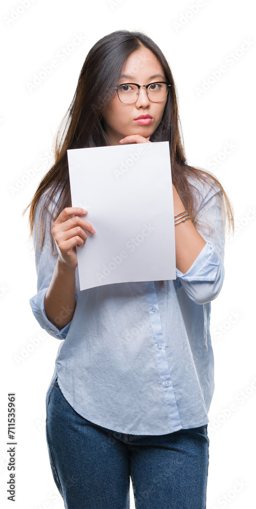 Young asian woman holding blank paper over isolated background serious face thinking about question, very confused idea