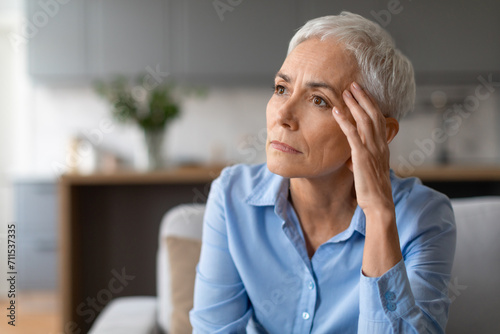 Portrait shot of unhappy european senior woman touching head indoor