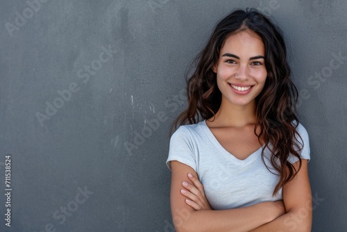 Smiling Latin woman with crossed arms on grey wall.