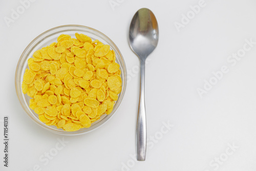 Corn flakes served in glass bowl with spoon on white with copy space