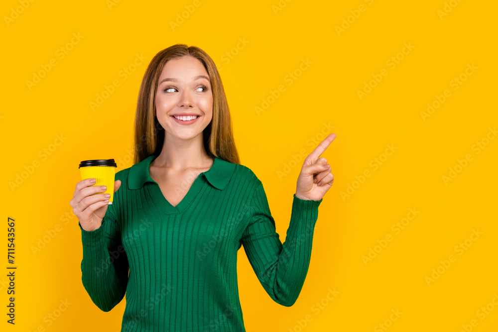 Portrait of young girl student holding tasty coffee direct finger empty space interested new news isolated on yellow color background Portrait of young girl student holding tasty coffee direct finger empty space interested new news isolated on yellow color background