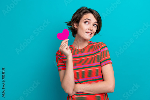 Photo of minded adorable woman dressed striped t-shirt hold paper heart dreamy look empty space isolated on turquoise color background