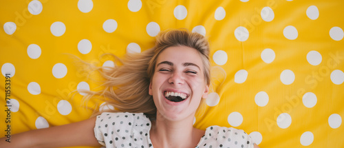 Mulher loira feliz deitada em um tapete amarelo com bolinhas brancas