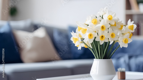 A vase with blooming daffodils on the coffee table in the living room against the background of the sofa. Easter, spring.