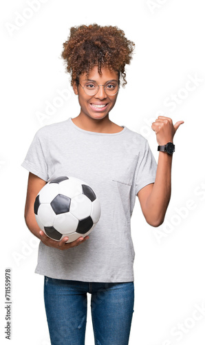 Young african american woman holding soccer football ball over isolated background pointing and showing with thumb up to the side with happy face smiling © Krakenimages.com