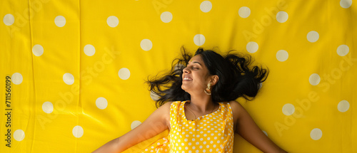 Mulher  indiana feliz deitada em um tapete amarelo com bolinhas brancas photo
