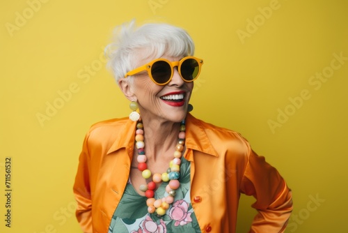 Cheerful senior woman in sunglasses looking at camera on yellow background