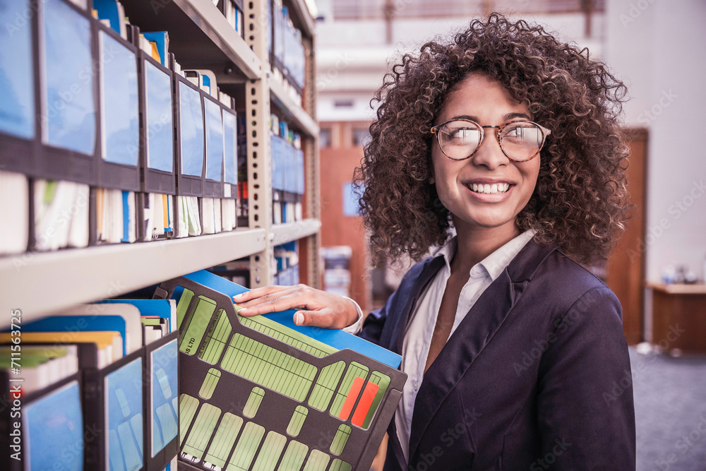 Young African corporate woman looking through shelves with binders and