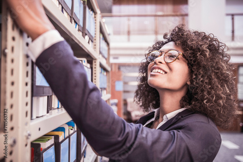 Young African corporate woman looking through shelves with binders and books in large start-up office space. Cape Town, South Africa