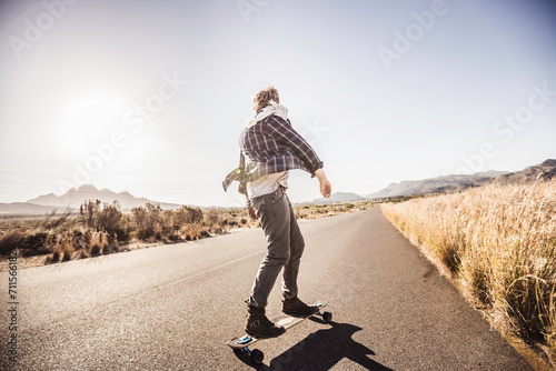Middle aged guy riding is skate board down straight road in the country side. Paarl, South Africa photo