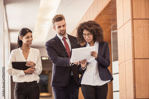 Mixed race colleagues working and brainstorming together while walking down a corridor in the office.