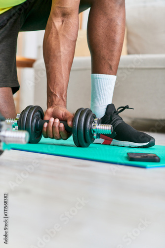 partial view of fit african american man in sportswear training with dumbbell in living room at home