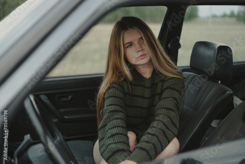 A redheaded girl in a green sweater sits in a retro car. The concept of free and cyclical fashion. © deine_liebe