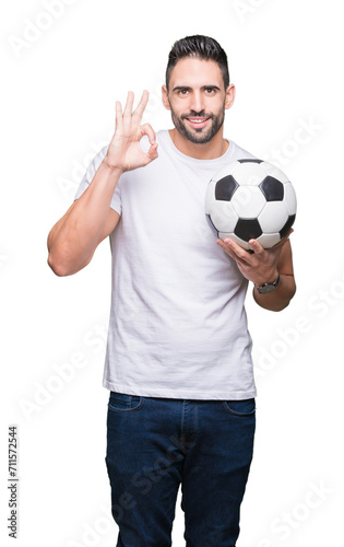 Young man holding soccer football ball over isolated background doing ok sign with fingers, excellent symbol