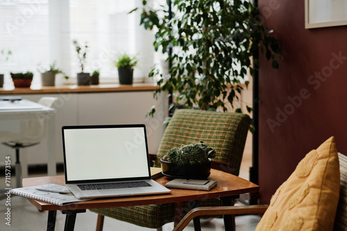 Laptop with white screen mockup placed on table in modern office with greenery and vintage furniture © AnnaStills