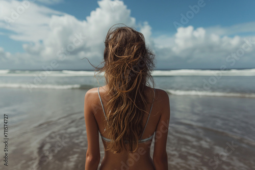 blonde woman in bikini standing at beach and looking at ocean waves. © Zenturio Designs