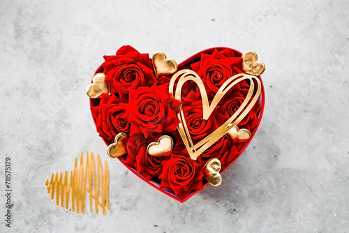 Valentine's day. Red roses and gold hearts in a heart-shaped box on a concrete background. A gift for women on a holiday. The concept of flower delivery. floristry and flower shops. photo