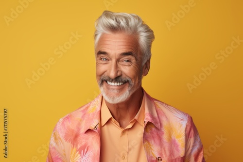 Portrait of smiling senior man looking at camera and standing against yellow background