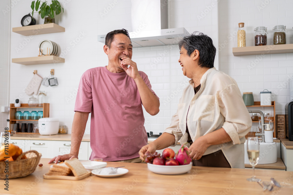 Mature asian Couples playfully tease each other with grapes in kitchen.