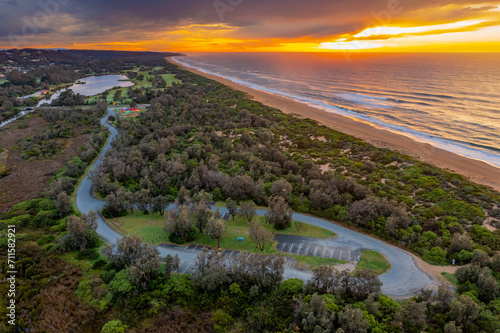 Aerial view over an empty coastal carpark, amongst trees with a dramatic sunrise overhead photo