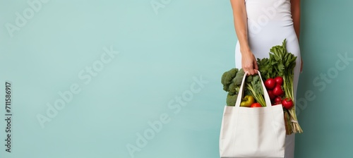 Eco friendly individual holding local produce in reusable tote bag on light blue background