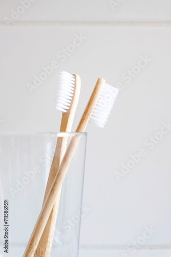 Stylish natural eco friendly toothbrushes with wooden bamboo handle in glass in bathroom. Oral hygiene concept. Copy space for text. Reduce plastic waste  sustainable lifestyle.