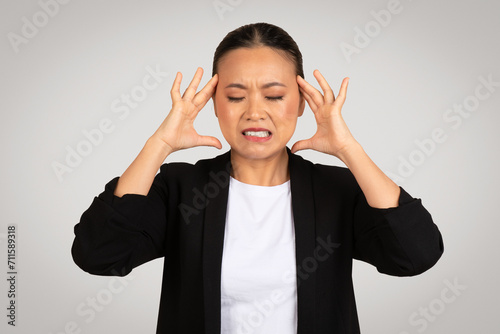 Stressed Asian businesswoman with a pained expression, holding her head in frustration or headache