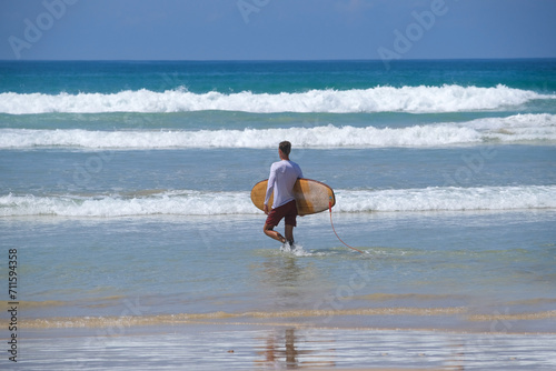 Surfer on the beach goes to the water with surf board