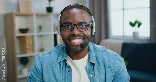 Portrait of handsome smiling man satisfied young bearded African American boy in glasses in earphones which looking into camera with friendly face expression photo