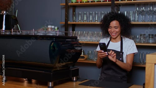 A dark-skinned young woman takes her phone out of her pocket in the middle shot and jumping. Take out your phone and be surprised. The barista took his phone out of his pocket in the coffee shop.