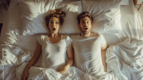 Top view shocked young couple two family man woman in casual white clothes lying in bed looking at each other rest relax spend time together in bedroom lounge home in own room house wake up good day