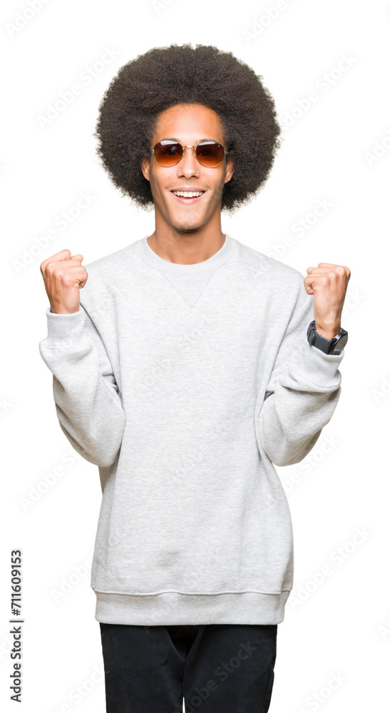 Young african american man with afro hair wearing sunglasses celebrating surprised and amazed for success with arms raised and open eyes. Winner concept. Young african american man with afro hair wearing sunglasses celebrating surprised and amazed for success with arms raised and open eyes. Winner concept.