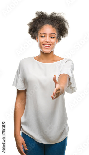 Young afro american woman over isolated background smiling friendly offering handshake as greeting and welcoming. Successful business.